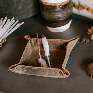 A leather tray with a feather and a vase.