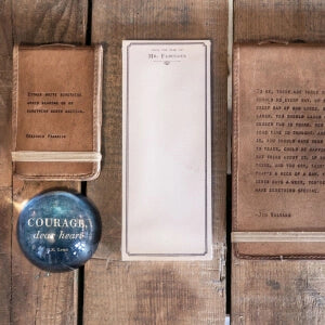 A notebook, pen, and book placed on a wooden table for studying or writing purposes.