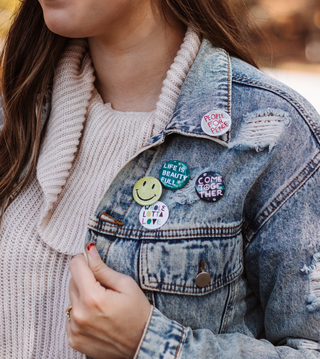 a person wearing a denim jacket with pins on it